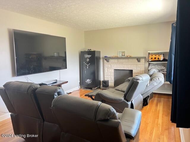 living room featuring a stone fireplace, a textured ceiling, and light wood-type flooring