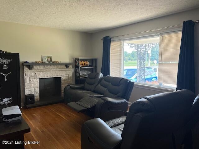 living room with a stone fireplace, dark hardwood / wood-style flooring, and a textured ceiling