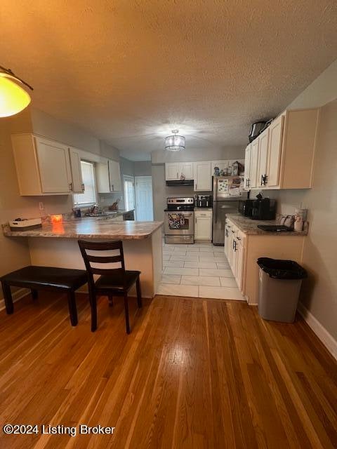 kitchen with kitchen peninsula, appliances with stainless steel finishes, a textured ceiling, light hardwood / wood-style flooring, and white cabinets