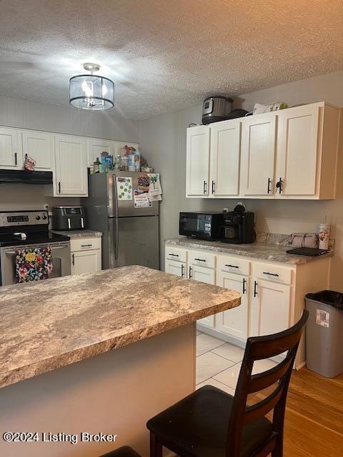 kitchen with stainless steel appliances, light hardwood / wood-style flooring, range hood, a textured ceiling, and white cabinets