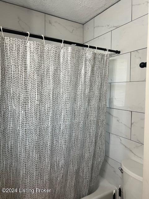 bathroom with shower / bath combo, a textured ceiling, and toilet