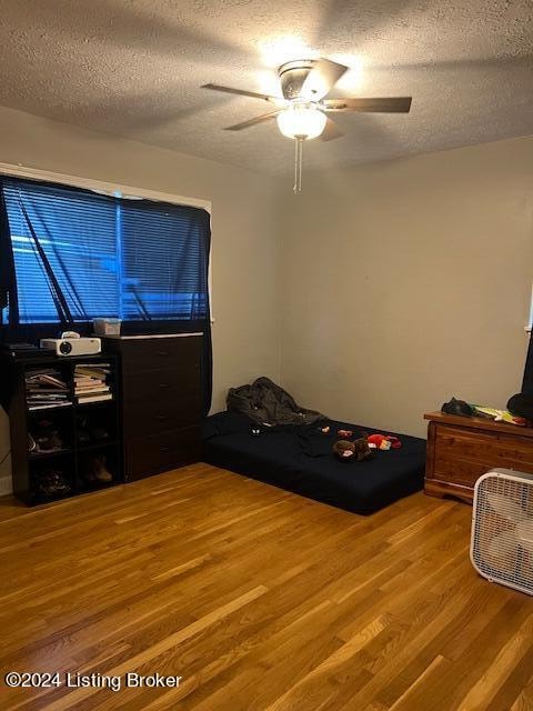 bedroom with ceiling fan, wood-type flooring, and a textured ceiling