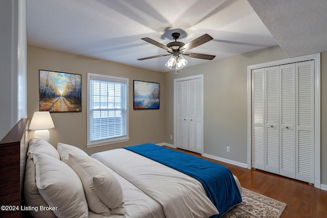 bedroom with ceiling fan, dark hardwood / wood-style flooring, and two closets