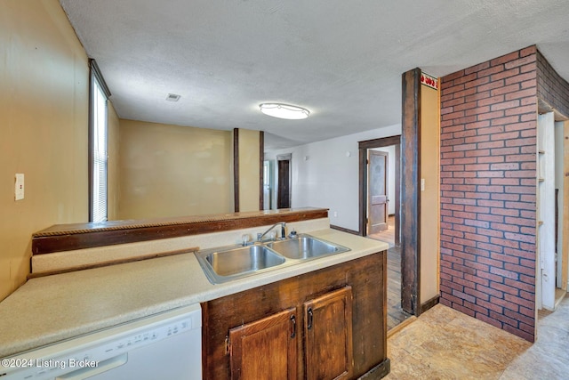 kitchen with white dishwasher, sink, brick wall, and a textured ceiling