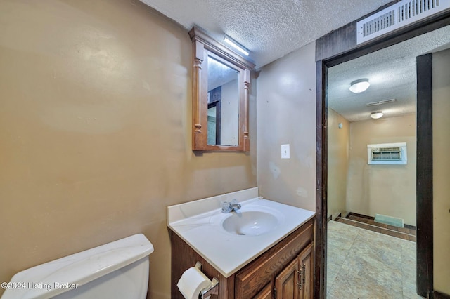 bathroom featuring vanity, toilet, an AC wall unit, and a textured ceiling