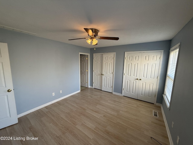 unfurnished bedroom with ceiling fan, light wood-type flooring, and multiple closets