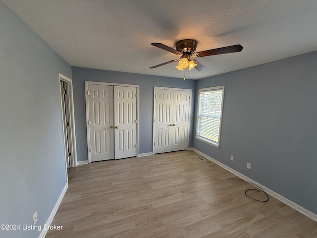 unfurnished bedroom with multiple closets, ceiling fan, and light wood-type flooring