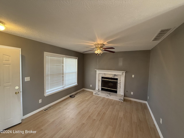 unfurnished living room featuring ceiling fan, light wood-type flooring, a textured ceiling, and a high end fireplace