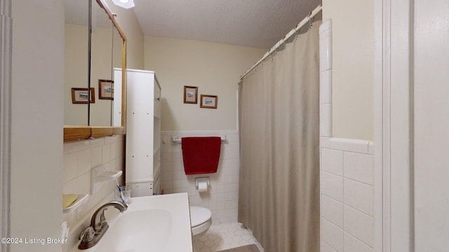 bathroom with a textured ceiling, sink, tile walls, and toilet