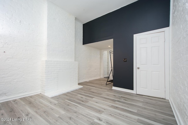 unfurnished room featuring light wood-type flooring and a brick fireplace