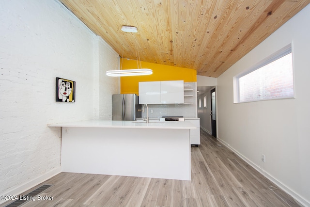 kitchen with stainless steel fridge, decorative light fixtures, light hardwood / wood-style flooring, white cabinetry, and lofted ceiling