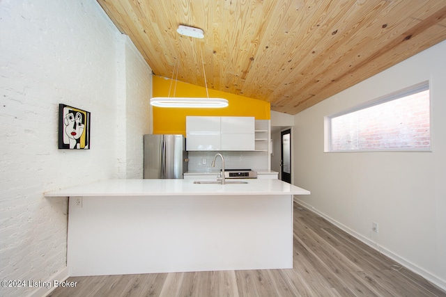 kitchen featuring white cabinets, sink, vaulted ceiling, decorative light fixtures, and stainless steel refrigerator