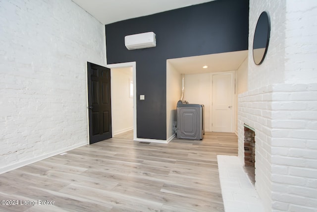 unfurnished living room featuring a fireplace, a high ceiling, light wood-type flooring, and a wall unit AC