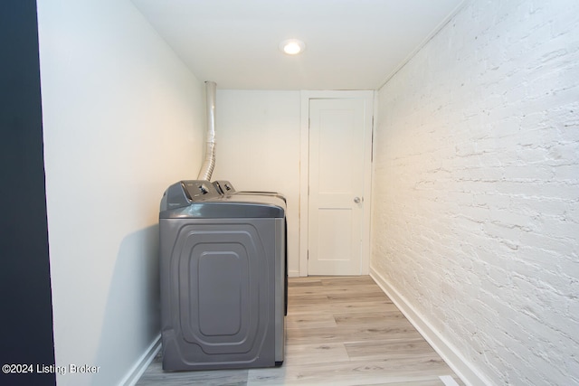 washroom with independent washer and dryer, light wood-type flooring, and brick wall