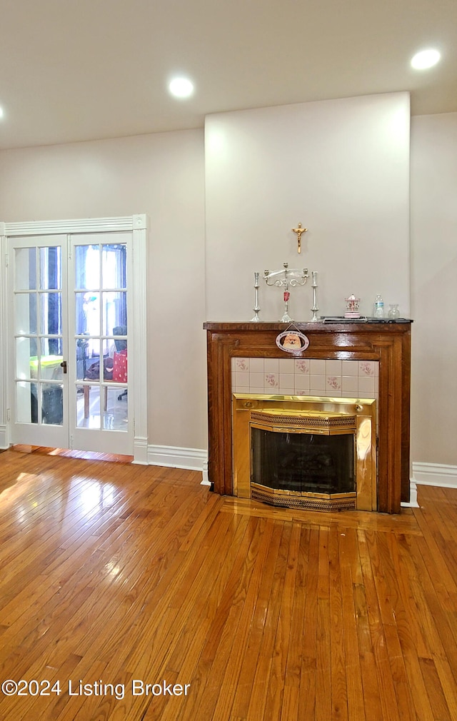 unfurnished living room with a tiled fireplace, hardwood / wood-style floors, and french doors