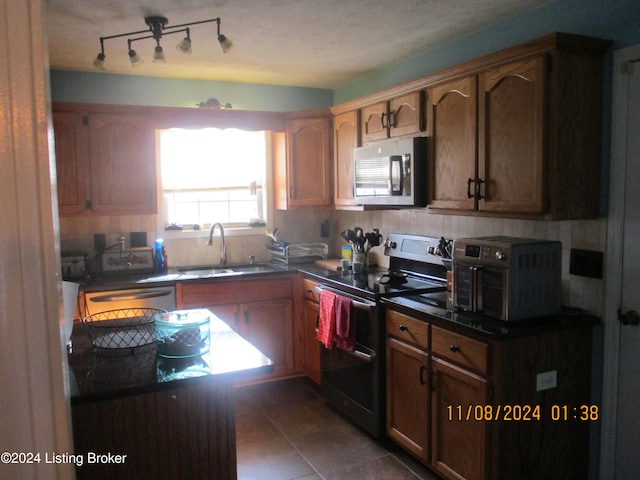 kitchen featuring sink, dark tile patterned floors, backsplash, a textured ceiling, and appliances with stainless steel finishes