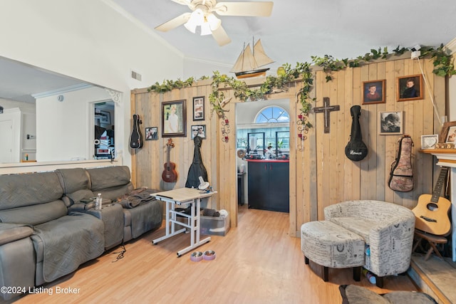 living room featuring ceiling fan, light wood-type flooring, ornamental molding, and wooden walls