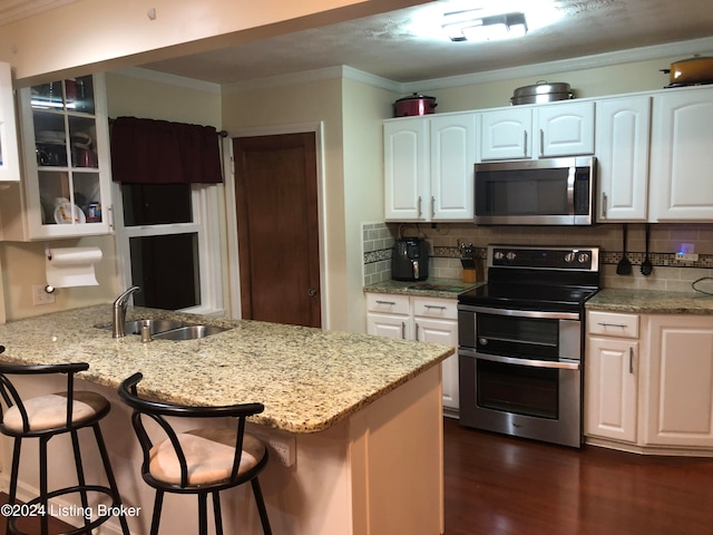 kitchen with appliances with stainless steel finishes, a kitchen breakfast bar, dark wood-type flooring, sink, and white cabinetry