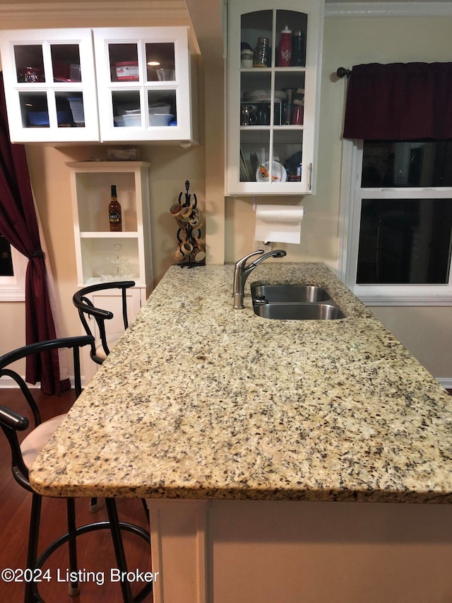 kitchen featuring sink, light stone counters, kitchen peninsula, a breakfast bar area, and hardwood / wood-style flooring