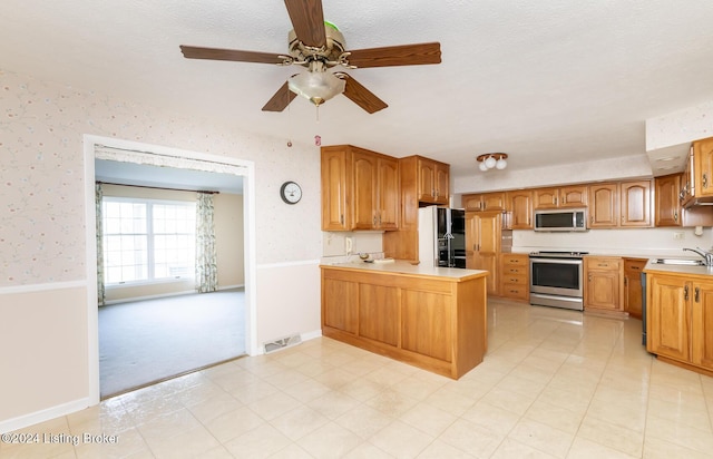 kitchen featuring ceiling fan, sink, kitchen peninsula, a textured ceiling, and appliances with stainless steel finishes