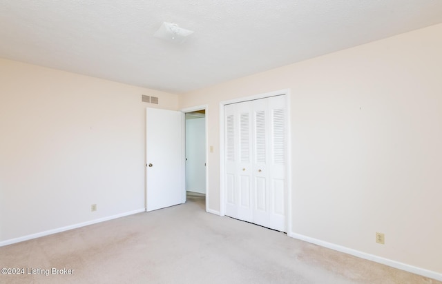 unfurnished bedroom featuring a textured ceiling, light carpet, and a closet