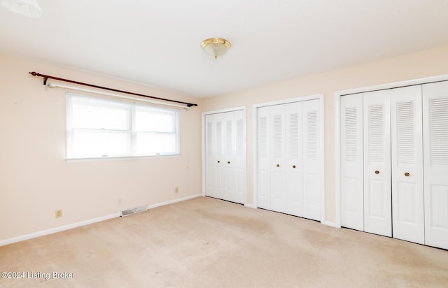 unfurnished bedroom with light colored carpet and multiple closets