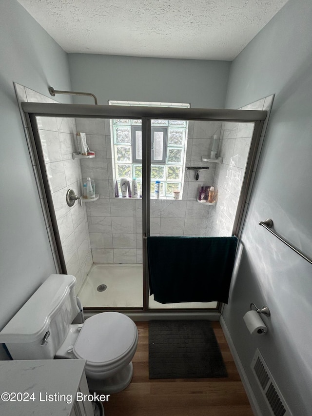 bathroom featuring hardwood / wood-style floors, an enclosed shower, a textured ceiling, and toilet