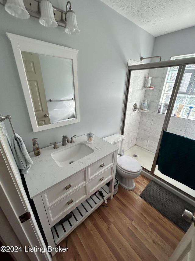 bathroom featuring a tile shower, wood-type flooring, a textured ceiling, toilet, and vanity