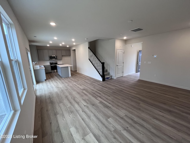 unfurnished living room with recessed lighting, wood finished floors, visible vents, baseboards, and stairs