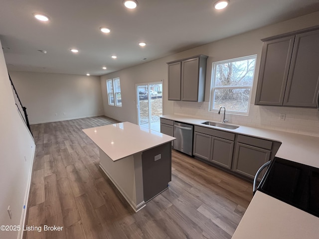 kitchen featuring dishwasher, wood finished floors, a center island, gray cabinets, and a sink