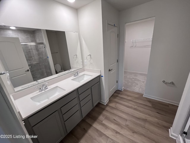 full bathroom featuring double vanity, a shower stall, a sink, and wood finished floors