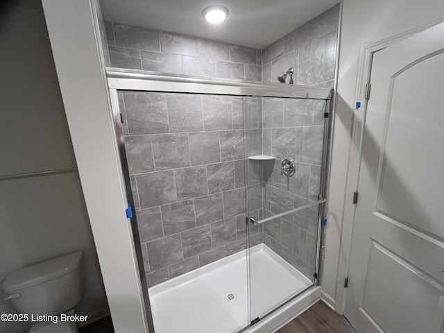 bathroom with a stall shower, toilet, and wood finished floors