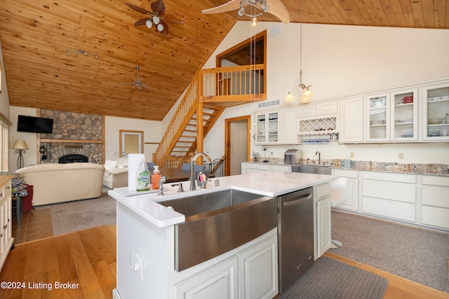 kitchen with light wood-type flooring, decorative light fixtures, dishwasher, white cabinetry, and a stone fireplace