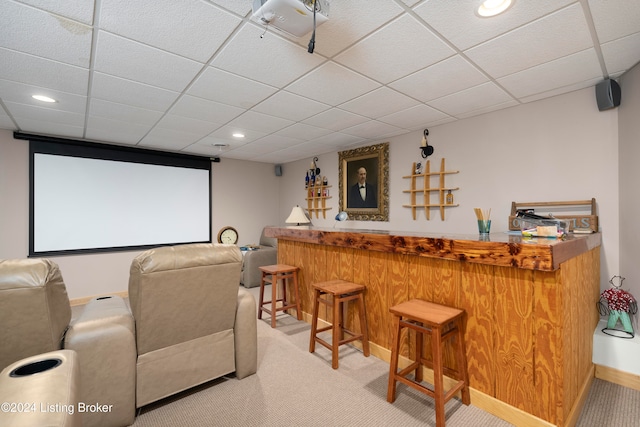 carpeted home theater room with a paneled ceiling and bar