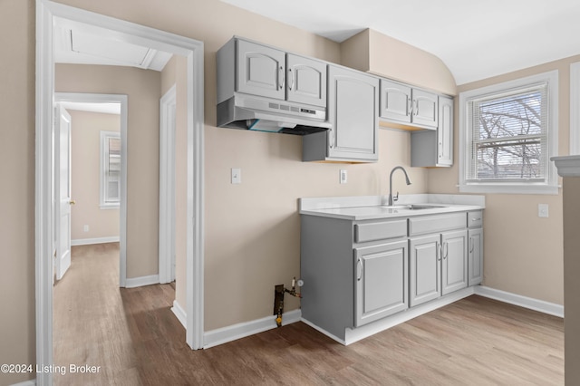 kitchen with gray cabinetry, sink, vaulted ceiling, and light hardwood / wood-style flooring