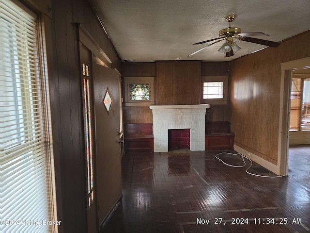 unfurnished living room with wooden walls, ceiling fan, a textured ceiling, a fireplace, and dark hardwood / wood-style flooring