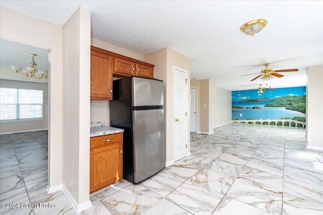 kitchen with a textured ceiling, stainless steel refrigerator, and ceiling fan with notable chandelier