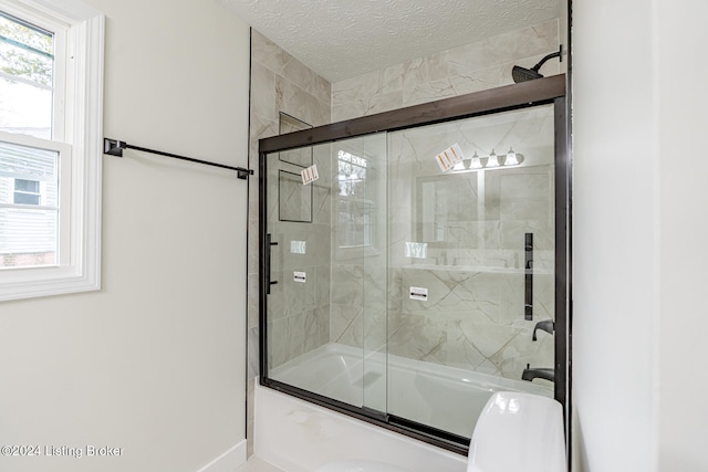 bathroom with combined bath / shower with glass door and a textured ceiling