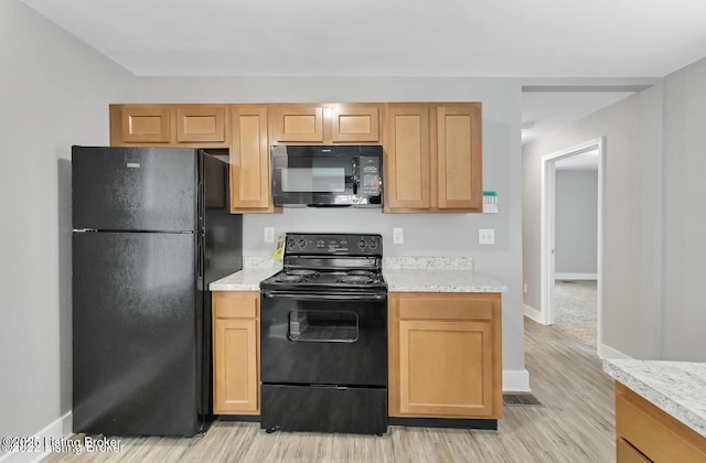 kitchen featuring light hardwood / wood-style floors, light stone counters, and black appliances