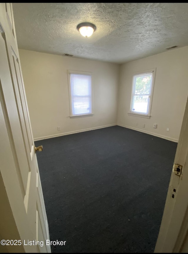 spare room with dark carpet and a textured ceiling