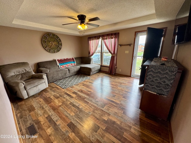 living room featuring hardwood / wood-style floors, ceiling fan, a raised ceiling, and a textured ceiling