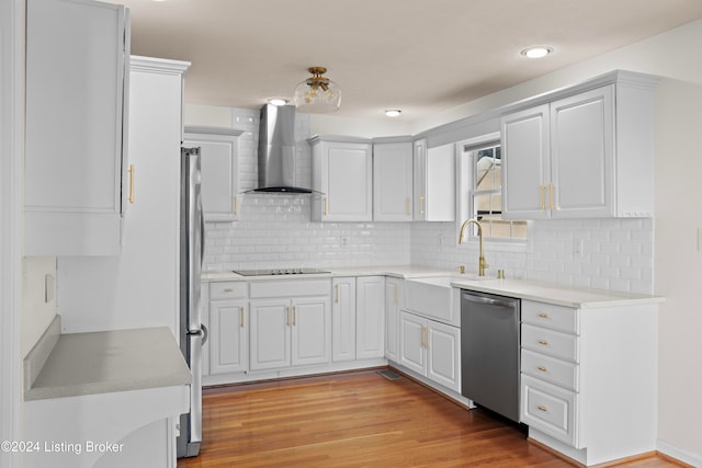 kitchen featuring white cabinetry, sink, stainless steel appliances, wall chimney range hood, and light hardwood / wood-style flooring