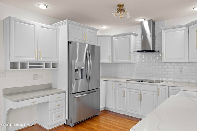 kitchen with white cabinets, wall chimney range hood, light hardwood / wood-style floors, light stone counters, and stainless steel fridge with ice dispenser