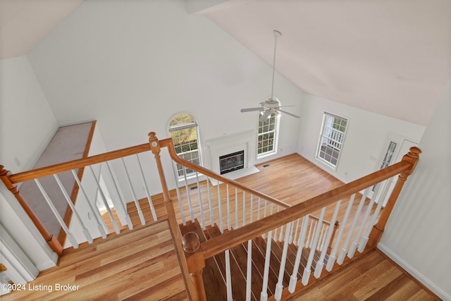 stairs with wood-type flooring, high vaulted ceiling, and ceiling fan