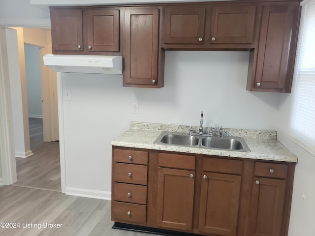 kitchen with light stone counters, light wood-type flooring, sink, and exhaust hood