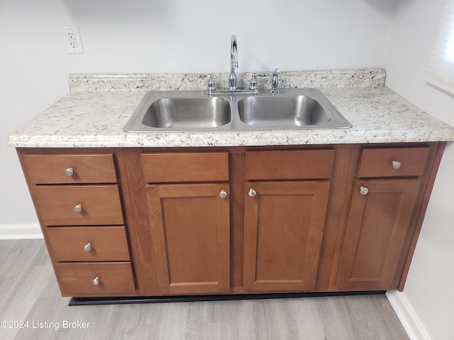 kitchen with light wood-type flooring, light stone counters, and sink