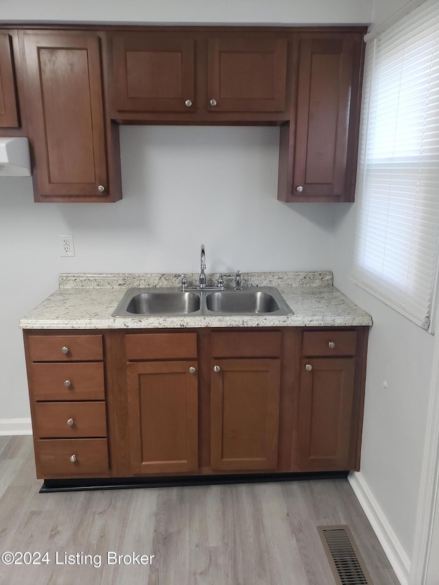 kitchen with light stone counters, sink, exhaust hood, and light wood-type flooring