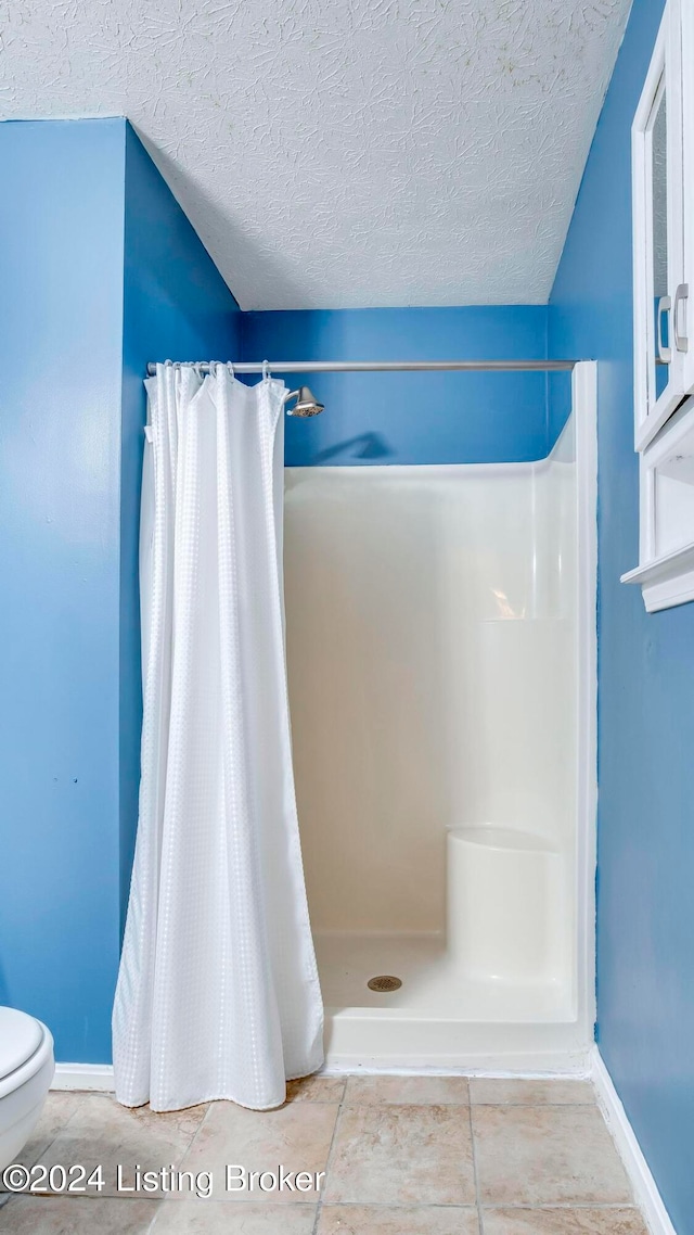 bathroom with tile patterned floors, toilet, a textured ceiling, and a shower with shower curtain