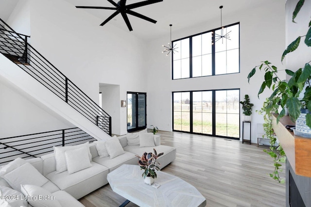 living room with light hardwood / wood-style flooring, a towering ceiling, and ceiling fan with notable chandelier