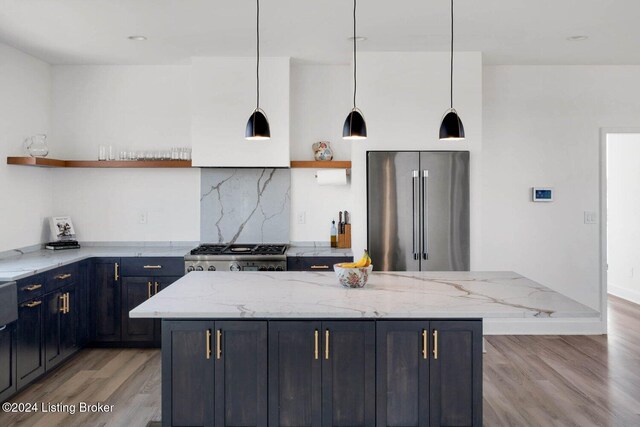 kitchen with light stone countertops, hanging light fixtures, stainless steel appliances, and light wood-type flooring